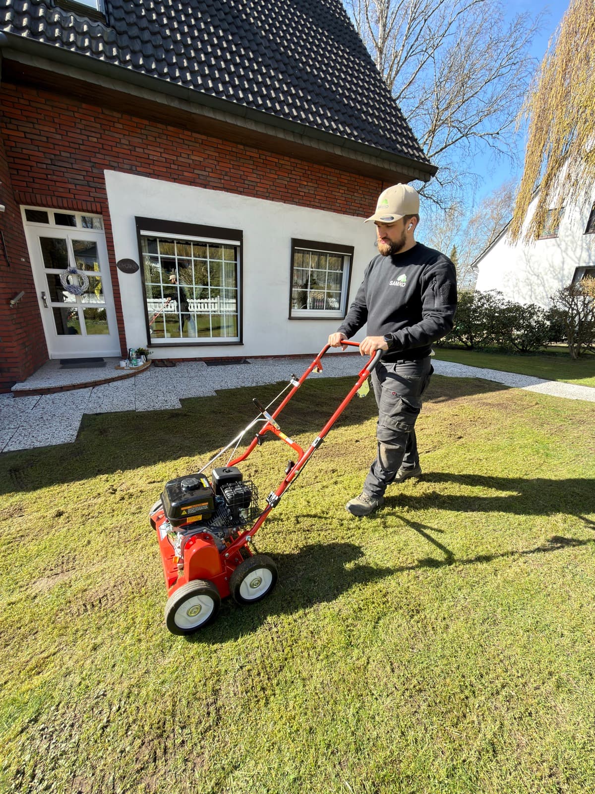 Vertikutieren des Rasens im Vorgarten eines Klinkerhauses